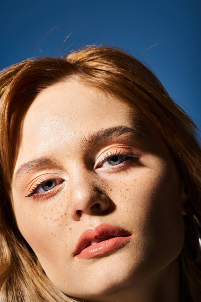 Closeup beauty shot of pretty woman with blue eyes, peach makeup and freckles on blue background - Fotó, kép