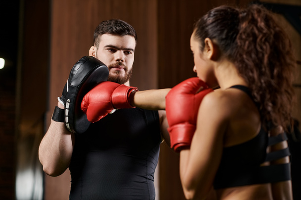 Un allenatore di sesso maschile allena una sportiva bruna mentre si impegnano in una partita di boxe in un ambiente di palestra. - Foto, immagini