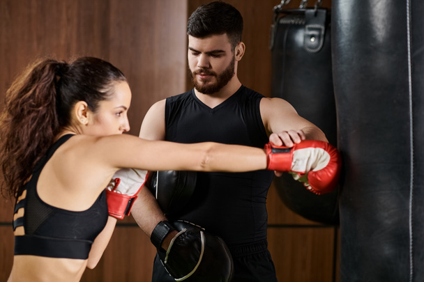 Męski trener stoi obok brunetki w rękawiczkach bokserskich, aktywnie trenując na siłowni. - Zdjęcie, obraz