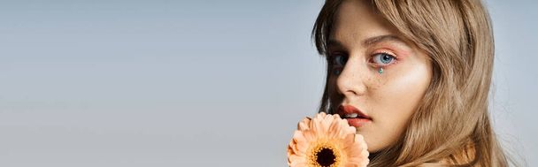 Closeup beauty shot of woman with peach makeup eyeliner, gerbera daisy, face jewels, banner - Photo, Image