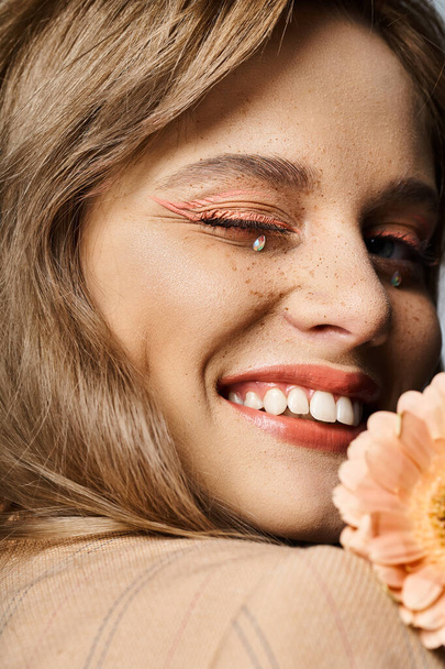 Closeup beauty shot of woman winking with peach makeup, gerbera daisy, face jewels and freckles - Photo, Image