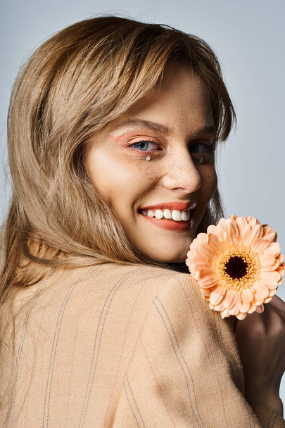 Back view portrait of woman smiling with peach makeup, gerbera daisy, face jewels and freckles - Foto, afbeelding