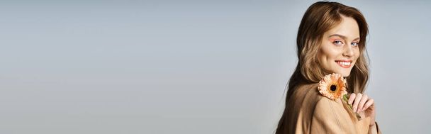 Привлекательная веселая женщина смотрит в камеру и держит маргаритку, носит персиковый макияж, плакат - Фото, изображение