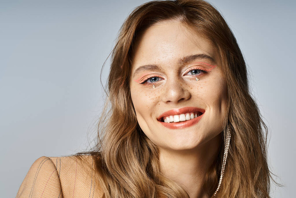 Портрет усміхненої жінки, що дивиться на камеру, одягнений в оголений персиковий макіяж та дорогоцінні камені для обличчя - Фото, зображення