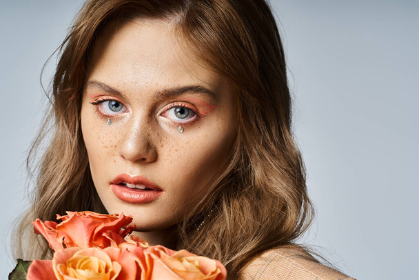 Beautiful woman with roses near her face and wearing nude peach makeup and sparkling face jewels - Fotó, kép