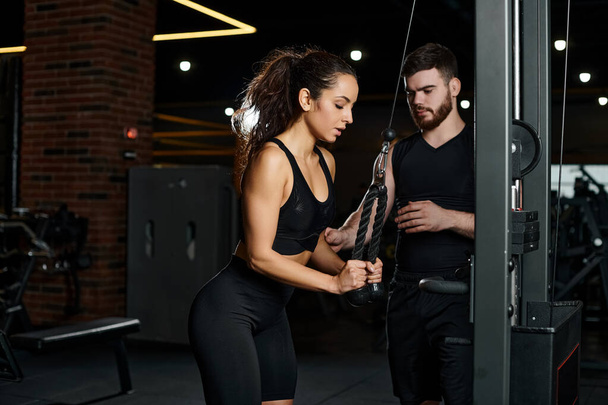Ein Personal Trainer führt eine brünette Sportlerin durch eine Workout-Routine in einem lebendigen Fitnessstudio. - Foto, Bild