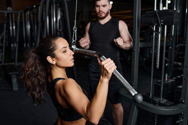 Ένας άντρας γυμναστής και μια μελαχρινή αθλήτρια γυμνάζονται μαζί σε ένα γυμναστήριο, συγκεντρωμένοι και αποφασισμένοι. - Φωτογραφία, εικόνα