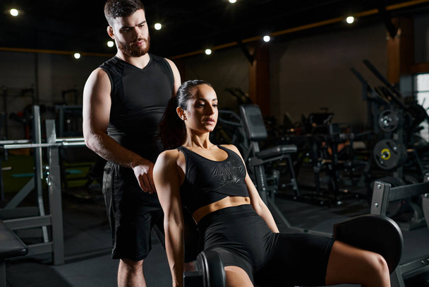 Mężczyzna trener stoi obok brunetki sportowej w siłowni, pomagając w rutynowym treningu. - Zdjęcie, obraz