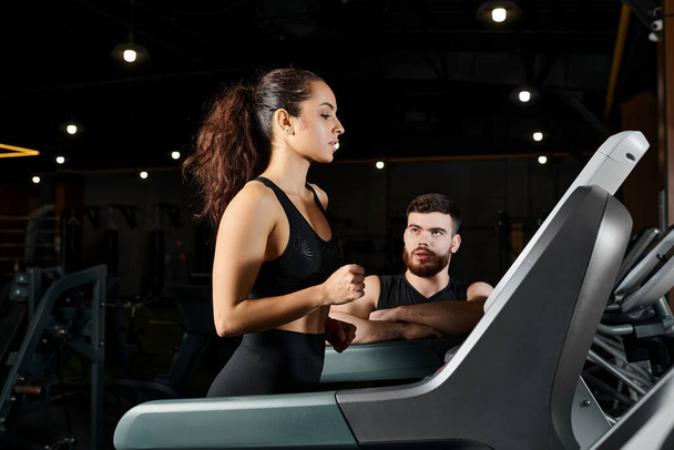 Um personal trainer masculino e uma esportista morena correndo energeticamente em uma esteira em um ginásio. - Foto, Imagem