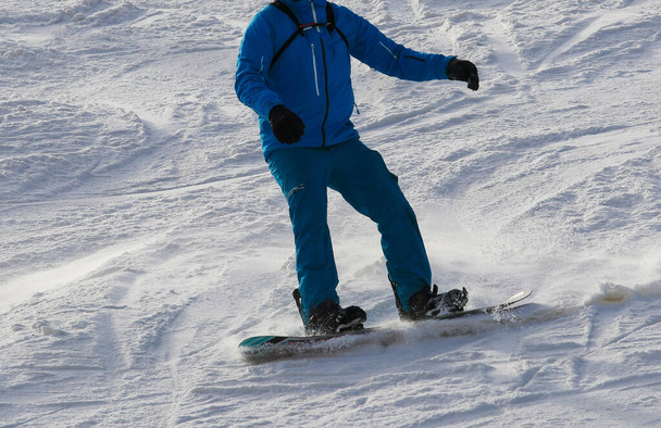Close up of a snowboarder skiing down a mountain wearing a blue coat and snow pants. - Photo, Image