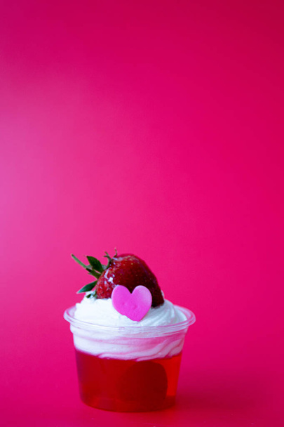 Galaretka truskawkowa z białym bitą śmietaną i świeżą truskawką z różowym sercem, czerwone tło - Zdjęcie, obraz