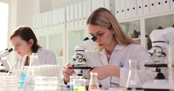 Moderni lääketieteellinen tutkimuslaboratorio naispuoliset tutkijat työskentelevät mikroskoopit. Biologien ryhmä analysoi tiedot ja käyttää mikroskooppia - Materiaali, video
