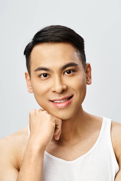 Ein gutaussehender asiatischer Mann strahlt in einem grauen Studio-Ambiente mit einem strahlenden Lächeln auf dem Gesicht Freude aus. - Foto, Bild