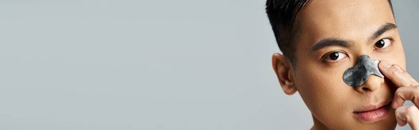 Portrét pohledného asijského muže s kosmetickou náplastí v šedém ateliéru. - Fotografie, Obrázek