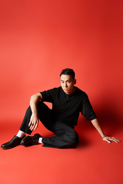 Schöner asiatischer Mann in stylischer schwarzer Kleidung sitzt mit überkreuzten Beinen auf dem Boden und strahlt Ruhe und Gelassenheit aus. - Foto, Bild