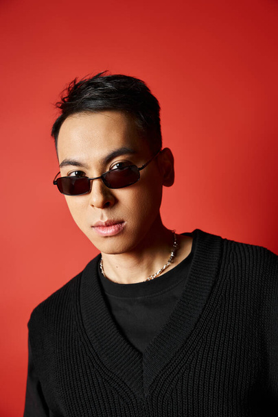 A handsome Asian man poses in a black outfit and sunglasses against a vibrant red backdrop. - Photo, Image