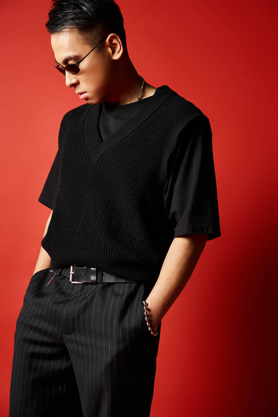 Stílusos, jóképű ázsiai férfi fekete ingben és nadrágban, magabiztosan áll egy vörös stúdióban.. - Fotó, kép