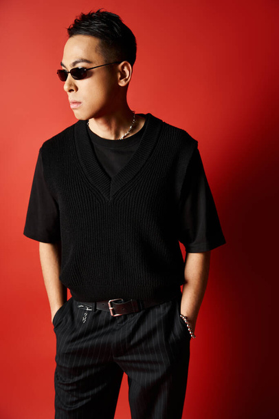 A stylish and handsome Asian man dressed in all black poses against a striking red background in a studio setting. - Photo, Image