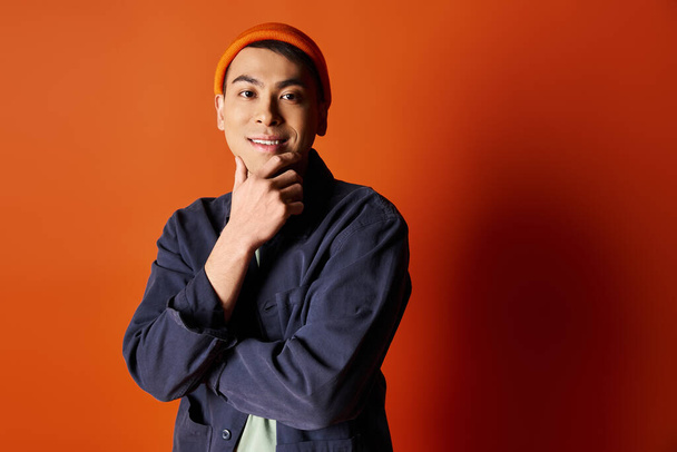 Ein gut aussehender asiatischer Mann in stilvoller Kleidung steht selbstbewusst vor einer orangefarbenen Wand. - Foto, Bild