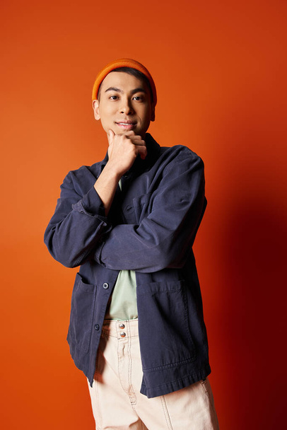 Un hombre asiático guapo se para con confianza frente a una pared naranja brillante con un atuendo elegante. - Foto, imagen