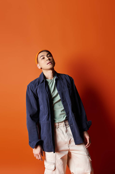 A handsome Asian man stands confidently in front of a striking orange wall in a stylish outfit. - Photo, Image