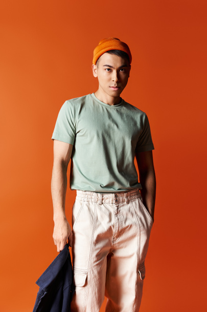 Jóképű ázsiai férfi turbánban magabiztosan áll egy élénk narancssárga háttér előtt egy stúdióban.. - Fotó, kép
