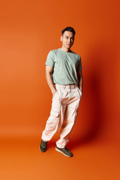 Een knappe Aziatische man in stijlvolle kleding staat vol vertrouwen voor een levendige oranje achtergrond, straalt verfijning en evenwicht uit. - Foto, afbeelding