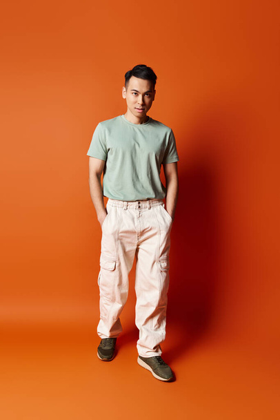 Yakışıklı Asyalı bir adam canlı turuncu bir duvarın önünde kendine güvenerek duruyor, stil ve bireysellik duygusu yayıyor.. - Fotoğraf, Görsel