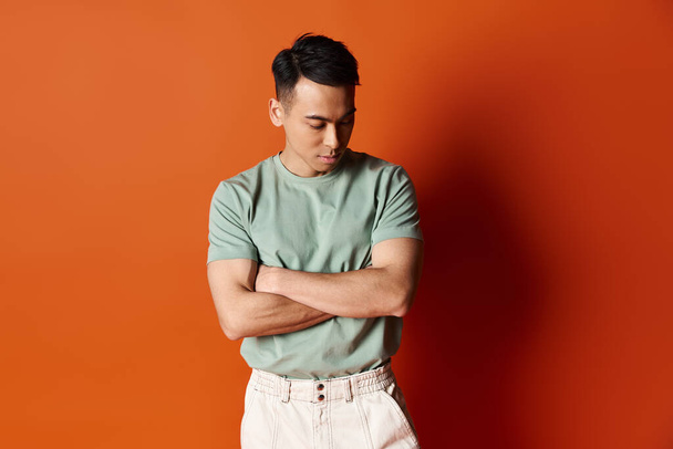 Un uomo asiatico elegante in abiti alla moda si erge con fiducia contro una parete arancione vibrante in uno studio. - Foto, immagini