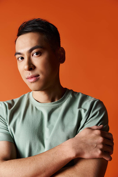 Handsome Asian man with crossed arms poses confidently in stylish attire against orange studio backdrop. - Photo, Image
