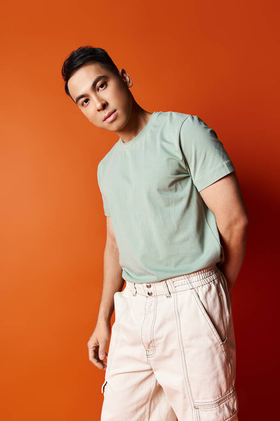 A handsome Asian man in stylish attire stands confidently in front of a vibrant orange wall in a studio setting. - Photo, Image