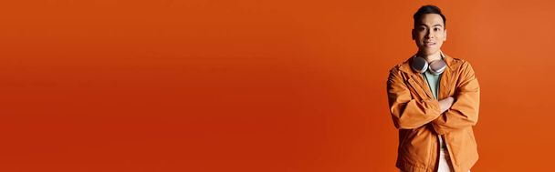Красивый азиат элегантно стоит в стильной одежде на ярком оранжевом фоне. - Фото, изображение