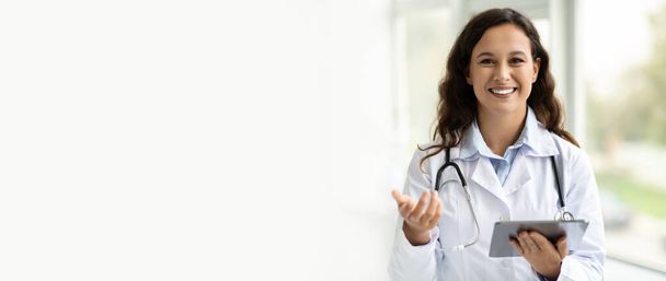 Усміхнена молода жінка-лікар у білому пальто працює на планшеті, позує в клініці, панорамі, копіює простір. Сучасний пристрій для віддаленої онлайн-консультації, новий звичай з медичною програмою - Фото, зображення
