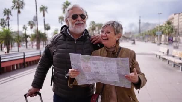 Starší kavkazský turistický pár, který se usmívá s cestovní mapou v rukou a hledá zajímavá místa. Starší manžel a manželka procházející se po ulici a užívající si dovolenou důchodců. Dospělí turisté  - Záběry, video