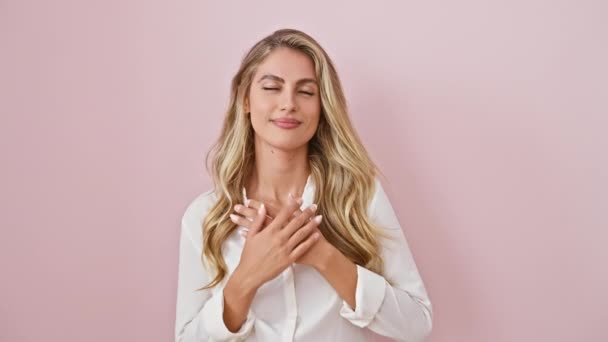 Vrolijke jonge blonde vrouw in roze, handen over de borst in teken van goede gezondheid, geïsoleerd staan met dankbaar gebaar, stralende hart-gevoelde vreugde en vertrouwen. - Video