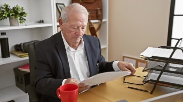 Senior man worker, ostřílený obchodní profesionál, intenzivně zaměřený, nosí brýle, čte zásadní kancelářský dokument na svém elegantním stole - Záběry, video
