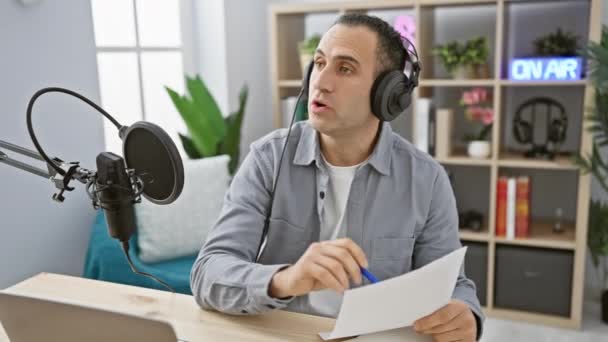 Egy fókuszált spanyol férfi fejhallgatóval mikrofonba beszél, egy rádiós stúdióban készülve egy adásra, aminek van egy felirata.. - Felvétel, videó