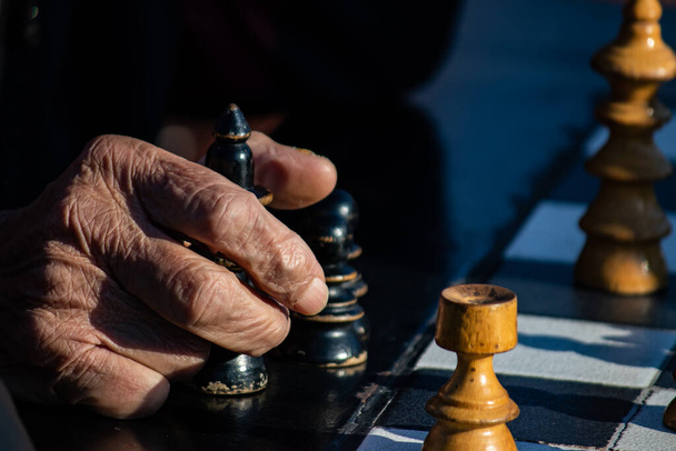 Руки літніх людей, які тримають шахові фігурки в громадському парку в Белграді, приємний сонячний день - Фото, зображення