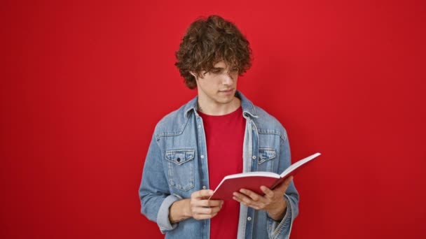 Alkalmi fiatalember göndör hajjal, farmerdzsekiben és piros ingben, könyvet olvas a vörös falnak, nyugodt, tanulságos hangulatot áraszt.. - Felvétel, videó