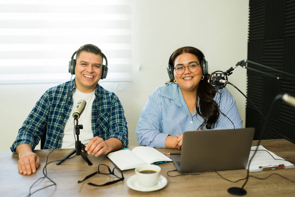 Vonzó nő és férfi mosolyog, miközben podcastet készít és beszél a mikrofonon lévő rádióműsor alatt, fülhallgatót viselve.  - Fotó, kép