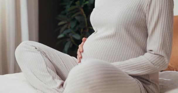 Verträumt lächelnde glückliche Frau inmitten ihrer Schwangerschaftsreise sitzt auf ihrem Bett und schätzt die Momente der Verbindung mit ihrem ungeborenen Baby, während sie zufrieden lächelt. - Filmmaterial, Video