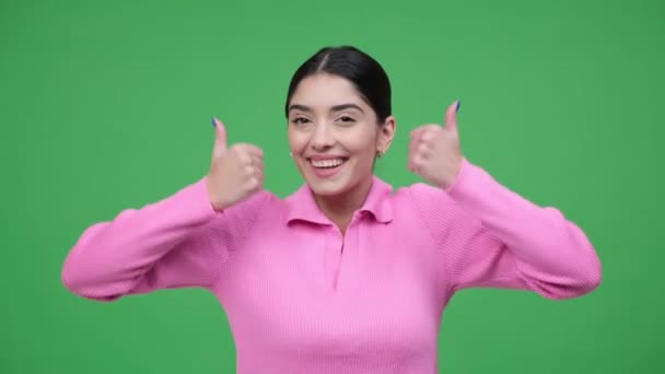 Mosolygó fiatal kaukázusi nő mutatja hüvelykujját felfelé, vagy mint jel és tánc, ünnepli győzelem, siker zöld háttérrel. Jóváhagyási mozdulat. - Felvétel, videó