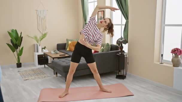 Una donna in forma esegue stretching yoga su un tappeto rosa in un soggiorno moderno con arredamento elegante. - Filmati, video