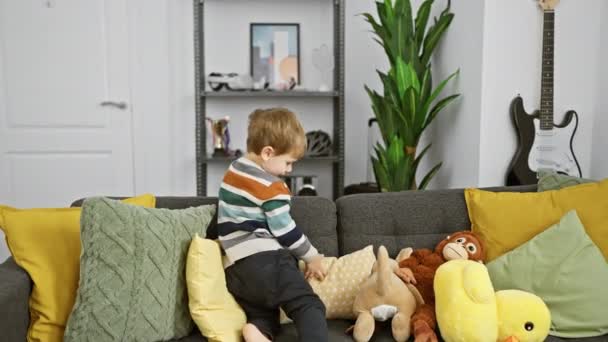 Adorabile bambino ragazzo seduto su un divano con giocattoli in un ambiente accogliente soggiorno - Filmati, video