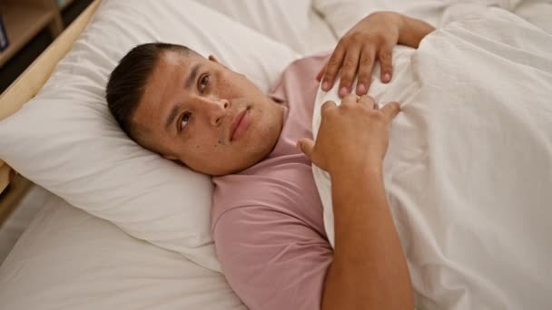 Verängstigter lateinischer Mann, der sein Gesicht mit einer Decke bedeckt, ängstlich im Bett in seinem Schlafzimmer liegt und Angst ausdrückt - Filmmaterial, Video