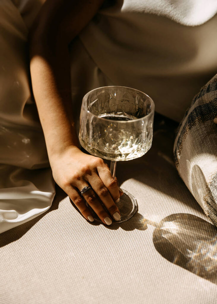 Una mano con anillo de compromiso de diamantes sosteniendo una copa de champán a la luz del sol. - Foto, imagen