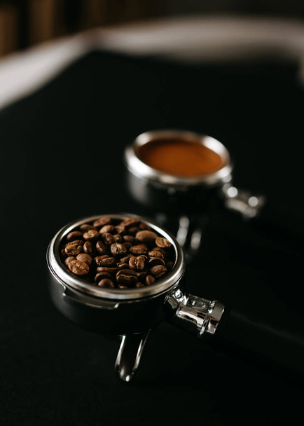 Dwa portafiltry espresso na czarnej powierzchni, jeden wypełniony ziarnem kawy, a drugi mieloną kawą. - Zdjęcie, obraz