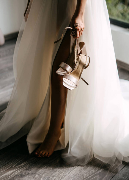Braut steht barfuß in eleganten Hochzeitsschuhen. - Foto, Bild