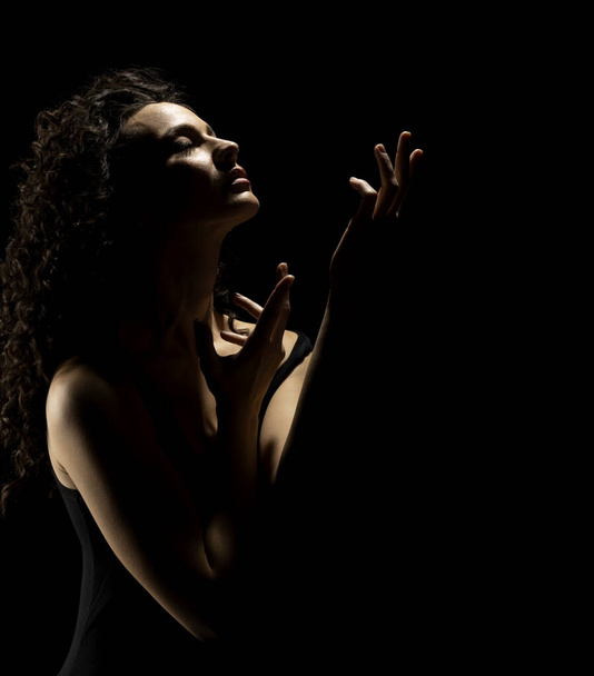 Zmysłowa sylwetka pięknej kręconej kobiety z wyciągniętą dłonią śpiewa w podświetleniu na czarnym tle studia - Zdjęcie, obraz