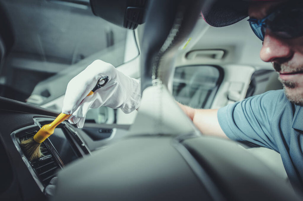 Szczegółowe sprzątanie wnętrza samochodu za pomocą profesjonalnych szczotek. Szczegółowy opis pojazdu wykonanego przez pracownika rasy kaukaskiej. - Zdjęcie, obraz